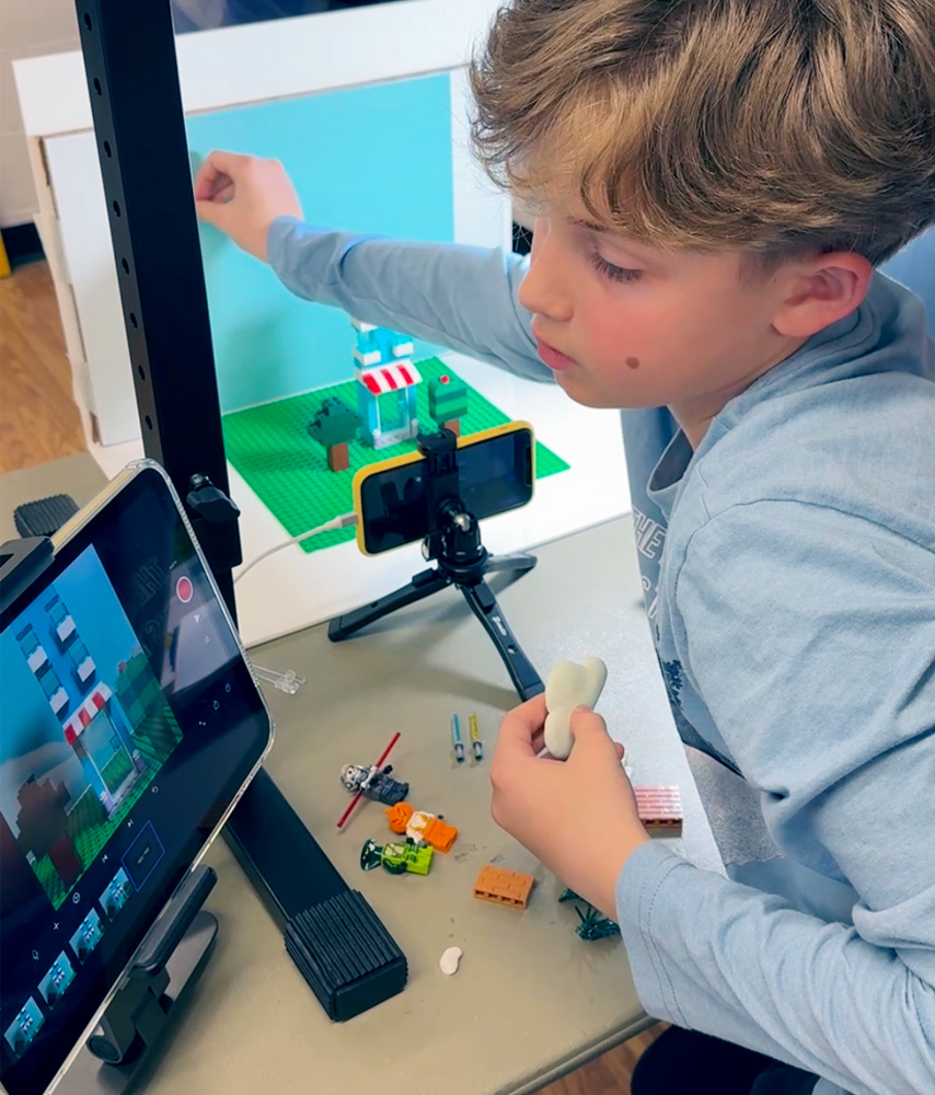 A child filming a stop-motion scene with a tablet and desk lamp in a Level 1 class