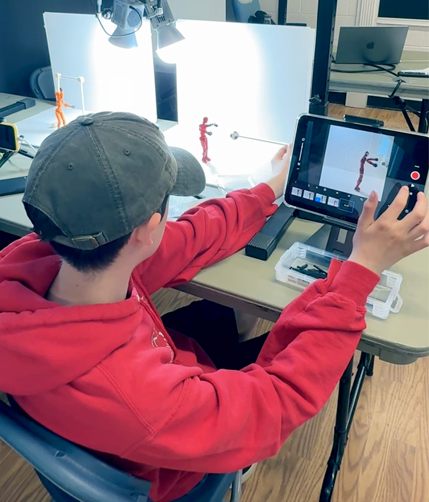 A student arranging paper cut-outs on a lightbox while filming a Level 2 stop-motion animation