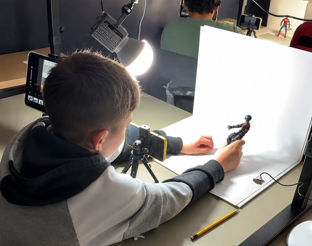 program icon A boy animating a small figure on a lit table with a tablet on a tripod